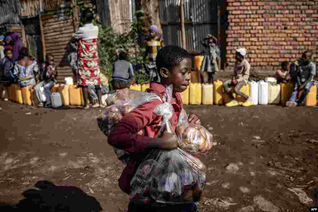 A boy sells snacks as residents queue with their water jars to collect water from a water point in Bukavu, Democratic Republic of Congo. (Photo by Luis TATO / AFP)