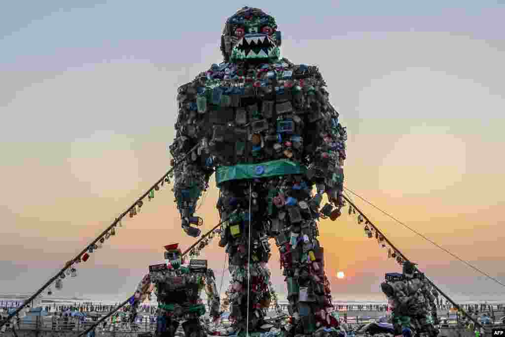 Orang-orang berjalan melewati patung raksasa 'Robot Monster' yang terbuat dari sampah-sanpah plastik untuk meningkatkan kesadaran tentang bahaya pencemaran plastik di laut, di pantai Cox's Bazar, Bangladesh.(AFP) 