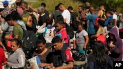 Migrantes esperan ser procesados por la Patrulla Fronteriza y de Aduanas de EEUU después de cruzar el Río Grande y entrar a EEUU desde México, el 19 de octubre de 2023, en Eagle Pass, Texas. 