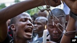 Un étudiant du Kenya porte chaînes maquettes et un autre tient une bougie pendant qu'ils marchent avec les autres commémorant la mémoire des victimes de l' attaque à l'université de Garissa. Ils protestent contre ce qu'ils disent être un manque de sécurité, dans le centre de Nairobi, au Kenya mardi 7 avril 2015.