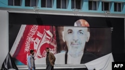 Dos hombres afganos se paran junto a un cartel rasgado del presidente afgano Ashraf Ghani en el aeropuerto de Kabul en Kabul el 16 de agosto de 2021.