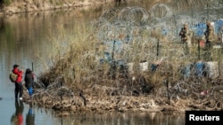 Una familia de migrantes habla con los miembros de la Guardia Nacional de EEUU después de cruzar el río Bravo en Eagle Pass, Texas, visto desde Piedras Negras, México, el 18 de enero de 2024.