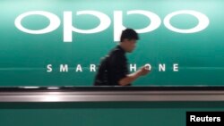 A commuter using his mobile phone passes an advertisement of Chinese smartphone maker Oppo at a train station in Singapore, May 8, 2014. 