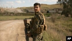 A U.S.-backed Syrian Democratic Forces fighter stands guard as trucks carrying Islamic State militants and families who surrendered in Baghuz, Syria, move to a camp, March 19, 2019. 