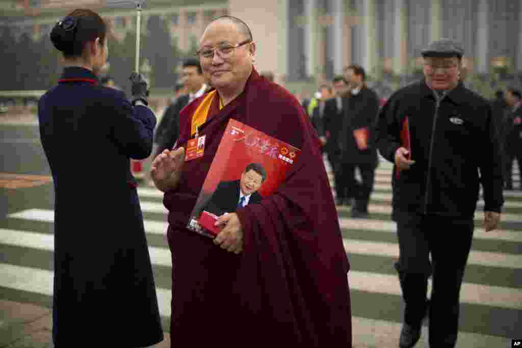 一个穿着喇嘛服装的代表在中国人民政治协商会议全体会议后离开北京人民大会堂,他携带一本《人民画报》,画报封面显示中国国家主席习近平。(2018年3月14日)