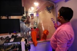 A woman looks at health workers as she gets ready to give nasal swab sample for COVID- 19 testing through rapid antigen methodology inside a mobile lab in New Delhi, India, Monday, Aug. 10, 2020. India is the third hardest-hit country by the…