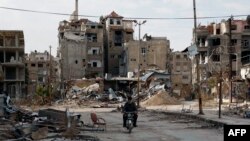 一名男子2月10日骑摩托车经过残破不堪的哈拉斯塔市（Harasta）。这座城市位于叙利亚首都大马士革以东。