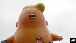 Una mujer vestida como la Estatua de la Libertad posa al lado del dirigible "Bebé Trump" mientras londinenses se reúnen para protestar contra la visita del presidente Donald Trump a Londres en junio del 2019.