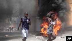 Manifestantes pasan corriendo junto a neumáticos incendiados durante una protesta contra la inseguridad en Puerto Príncipe, Haití, el 7 de agosto de 2023.