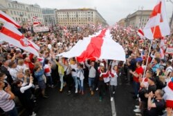 Demonstrators carry a huge historical flag of Belarus as thousands gather for a protest challenging official presidential election results, at Independence Square in Minsk, Belarus, Aug. 23, 2020.