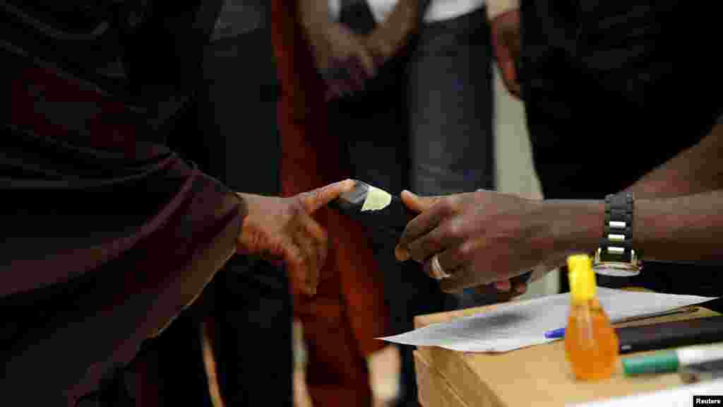 Un agent électoral scanne l'empreinte du pouce d’une électrice avec un appareil dans un bureau de vote au début des élections générales en Daura, au nord-ouest du Nigeria, samedi 28 mars 2015.