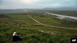 FILE - In this file photo dated May 1, 2019, a woman and child sit on a hill overlooking the Euphrates River as families picnic on May Day, in Derik, Syria.