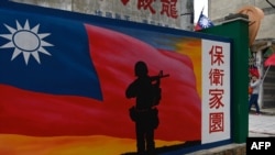 Seorang turis (kanan) berjalan melewati mural yang dilukis di dinding di Kepulauan Kinmen Taiwan, yang terletak hanya 3,2 km (dua mil) dari pantai China daratan (di latar belakang) di Selat Taiwan, 21 Oktober 2020. (Foto: AFP)
