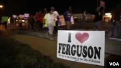 Sebuh tanda berbunyi "Saya Cinta Ferguson" sementara pada latar belakang tampak para pengunjuk rasa berjalan di kota Ferguson (21/8/2014). 