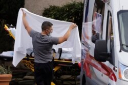 A man blocks the view as a person is taken by a stretcher to a waiting ambulance from a nursing facility where more than 50 people are sick and being tested for the COVID-19 virus, Saturday, Feb. 29, 2020, in Kirkland, Wash.