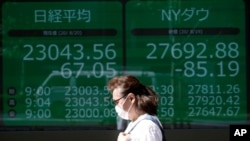 Seorang perempuan berjalan di papan elektronik yang menunjukkan indeks Nikkei 225 Jepang dan indeks Dow Jones (foto: ilustrasi). 