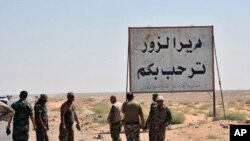 Pasukan Suriah dan pria bersenjata pro-pemerintah yang berdiri di samping sebuah plakat dalam bahasa Arab yang berbunyi, "Deir el-Zour menyambut Anda," di kota timur Deir el-Zour, Suriah, 3 September 2017. (SANA via AP).
