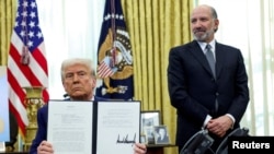 Президент США Дональд Трамп держит в руках указ о повышении пошлин в присутствии министра торговли США Говарда Латника. Овальный кабинет Белого дома. 13 февраля 2025 года. REUTERS.