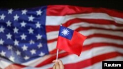 资料照片：在香港举行的台湾国庆游行中，一名反政府抗议者在飘扬的美国国旗前手持台湾国旗。(2019年10月10日)