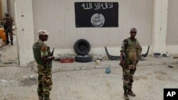 Chadian soldiers stand at a checkpoint in front of a Boko Haram flag in the Nigerian city of Damasak, March 18, 2015.