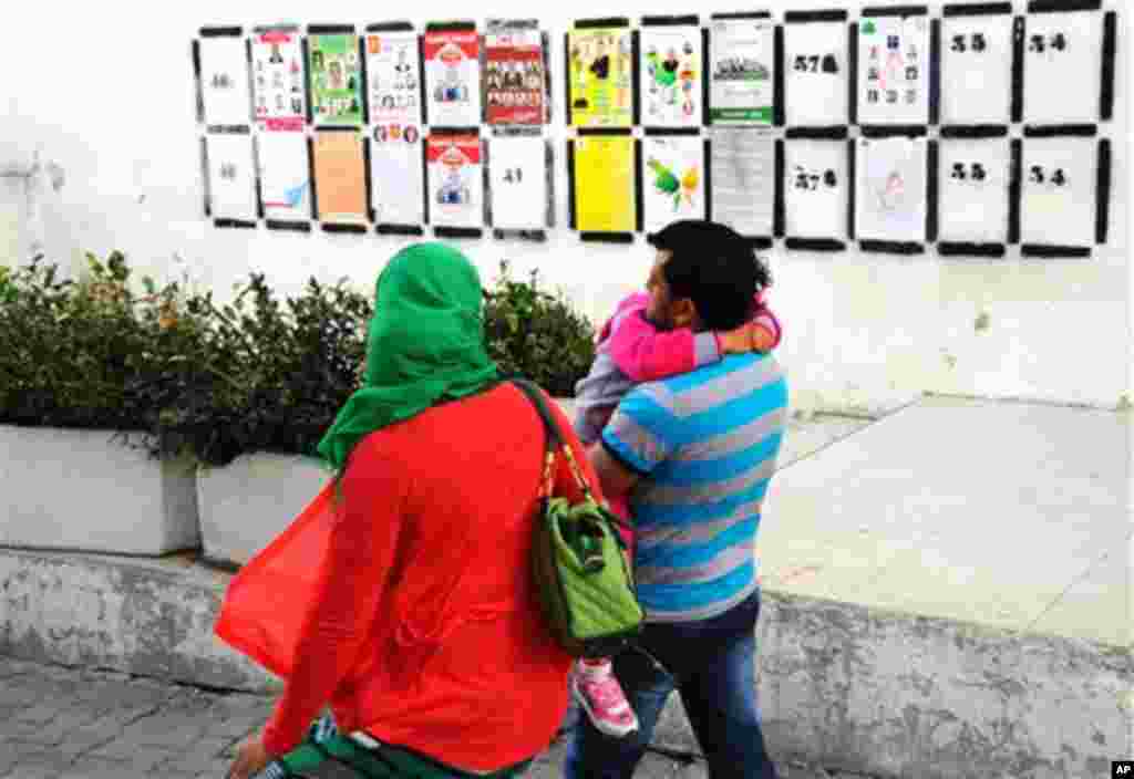 Sur cette photo datée du mercredi 22 octobre 2014, un couple passe près des affiches de la campagne électorale pour les prochaines élections législatives à Tunis, Tunisie. Les Tunisiens vont aller aux urnes le dimanche 26 octobre 2014.
