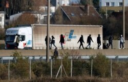 FILE - Migrants walk past a truck on the road that leads to the Channel Tunnel crossing in Calais, France, Dec.16, 2020.