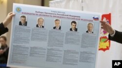 Russian election officials hold an election poster with portraits of the presidential candidates, Feb. 7, 2012.