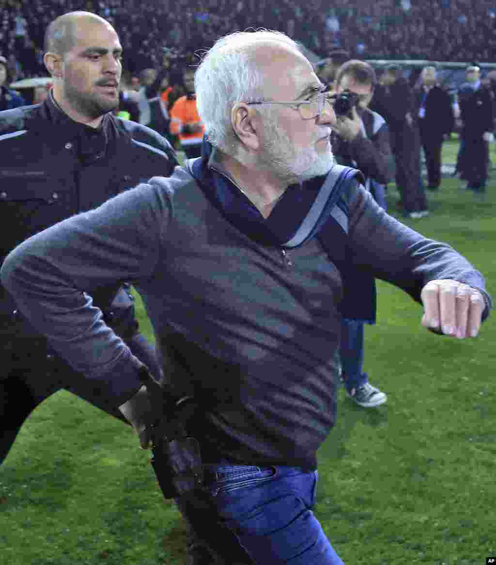 Mai kungiyar PAOK, Ivan Savvidis, rataye da bindiga a kunkuminsa, tare da masu gadinsa, a lokacin da ya kutsa cikin filin wasa a karawarsu da AEK Athens ranar lahadai a birnin Thessaloniki. Sau biyu Savvidis yana kutsawa cikin filin a lokacin wasa. Jami'an AEK sun yi zargin cewa Savvidis yayi barazana ga alkalin wasan a kutsawarsa ta farko, kafin masu gadinsa su janye shi. A karo na biyu an ga bindiga a rataye a kunkuminsa.(InTime Sports via AP)