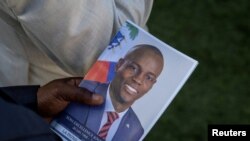 Una persona sostiene una foto del difunto presidente haitiano Jovenel Moise, quien fue asesinado a tiros el año pasado, durante su funeral en la casa de su familia en Cabo Haitiano, Haití, el 23 de julio de 2021.