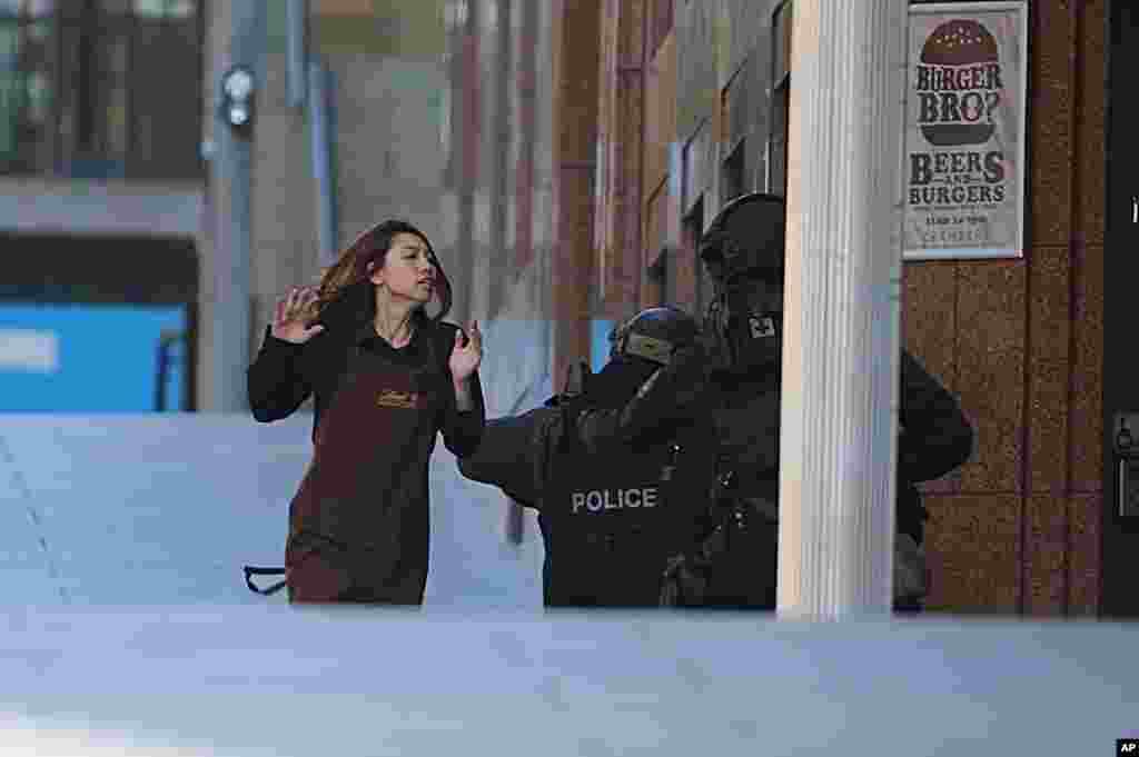 An armed tactical response police officer grabs a hostage as she flees from a cafe under siege at Martin Place in the central business district of Sydney, Australia, Dec. 15, 2014.