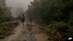 ARCHIVO - Mujeres caminan en el barro entre árboles talados hacia Comasagua, El Salvador, el lunes 10 de octubre de 2022.