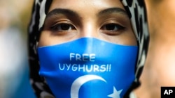 FILE - A woman wears a face mask reading 'Free Uyghurs' as she attends a protest during the visit of Chinese Foreign Minister Wang Yi in Berlin, Sept. 1, 2020. 
