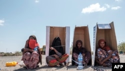 Pengungsi perempuan duduk di bawah kotak kardus bertuliskan Badan PBB urusan Pengungsi (UNHCR) saat mereka menunggu didaftarkan oleh pihak berwenang di kompleks Hotel Agda, kota Semera, wilayah Afar, Ethiopia, 14 Februari 2022. (EDUARDO SOTERAS / AFP)