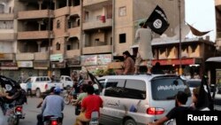 សមាជិក​ក្រុម Islamic State in Iraq and the Levant (ISIL) គ្រវី​ទង់ ISIL ខណៈ​ដែល​ពួក​គេ​​បើក​រថយន្ត​ក្នុង​ក្រុង Raqqa ប្រទេស​អ៊ិរ៉ាក់​កាល​ពី​ថ្ងៃ​ទី​២៩​ខែ​មិថុនា​ឆ្នាំ​២០១៤។