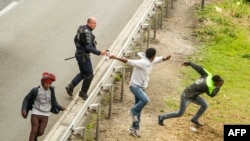 Police officer sprays tear gas at migrants trying to access Channel Tunnel on the A16 highway in Calais, northern France, June 23, 2015.