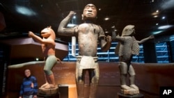 Visitors look at wooden royal statues from the Dahomey kingdom, dated 19th century, at the Quai Branly museum in Paris, Nov. 23, 2018.
