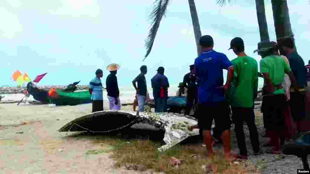 People stand next to a piece of suspected plane wreckage which has been found off the coast of southern Thailand in Nakhon Si Thammarat province, Jan. 24, 2016.