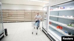 Un cliente empuja su carrito junto a los estantes vacíos en una tienda de Sainsbury's durante el brote de COVID-19, en Harpenden, Reino Unido, el 18 de marzo de 2020.
