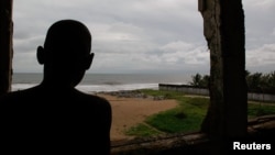 FILE - A young boy looks out from the window of his dilapidated home on the beach facing the Atlantic Ocean where his family lives in Monrovia, Liberia.