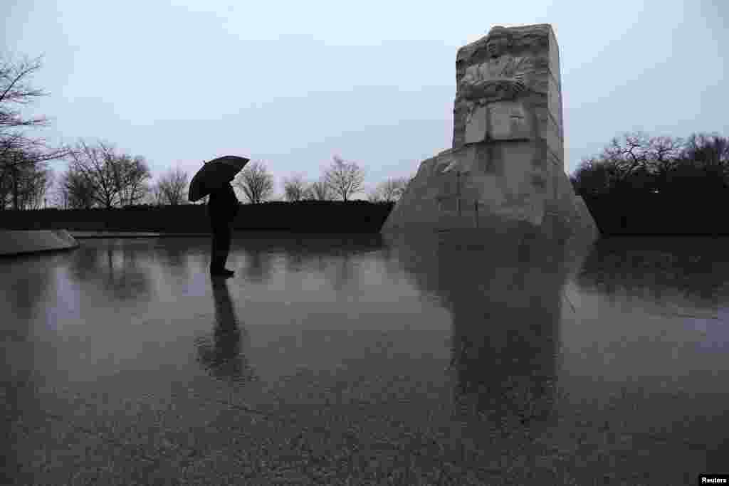 Di bawah payung dan hujan yang tak kunjung henti, seorang warga AS memberi penghormatan di Memorial Martin Luther King, Jr. di Washington (18/1). (Reuters/Jonathan Ernst)
