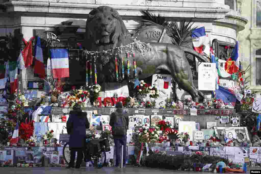 People look at flowers and other tributes to victims of last year's January and November shooting attacks near the statue at the Place de la Republique in Paris, France, January 6, 2016.
