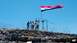 En esta foto de archivo del 17 de julio de 2018, publicada por la agencia oficial de noticias siria SANA, tropas sirias muestran un letrero de victoria junto a la bandera siria en Tell al-Haara, la colina más alta de la provincia suroccidental de Daraa, Siria. Israel derribó un avión de combate sirio que, según dijo, había roto su espacio aéreo el martes, cuando las fuerzas sirias llegaron a la frontera de los Altos del Golán por primera vez en siete años.