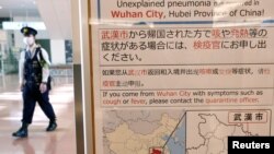 日本東京羽田機場一名戴著口罩的警察走過武漢肺炎的防疫廣告牌。（2020年1月20日） 