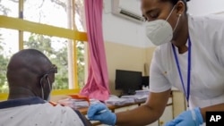 Khamis Juma, kiri, menerima suntikan vaksin virus corona 'Covishield' yang diproduksi oleh Serum Institute of India, dari perawat Amelie Richmond, kanan, di sebuah rumah sakit di ibu kota Victoria, Pulau Mahe, Seychelles Rabu, 24 Februari 2021 (Foto: AP)