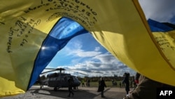Глядачі з українським прапором стоять біля гелікоптера Black Hawk у парку Летна під час презентації проекту «Подарунок для Путіна» у Празі, Чехія, 17 листопада 2023 року.