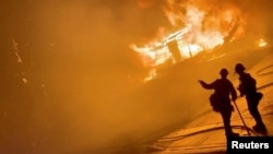 Dua orang petugas pemadam kebakaran di depan sebuah rumah yang terbakar di San Bernardino, California, 31 Oktober 2019.