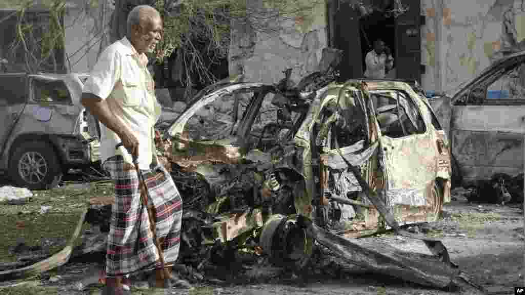 Un passant devant une voiture calcinée après l'explosion à l'hôtel de Mogadiscio, 2 juin 2016.