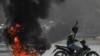 Hombre saluda junto a neumáticos en llamas durante una protesta contra el golpe militar, en Mandalay.