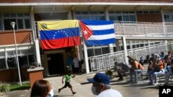 Frente a sendas banderas de Venezuela y Cuba, un chico corre mientras un grupo de personas espera recibir su vacuna contra el COVID-19, en la barriada Ciudad Tiuna, en Caracas, el 29 de junio de 2021.