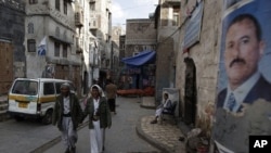 People walk along a street where posters hang of Yemen's President Ali Abdullah Saleh in the old city of Sanaa, Yemen, August 7, 2011